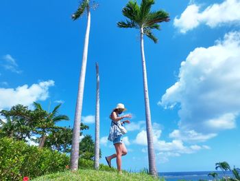 Woman standing by palm trees against blue sky