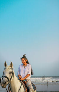 Woman riding horse in sea against clear sky
