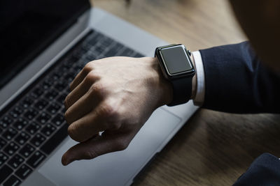 Cropped hand of man checking time against laptop