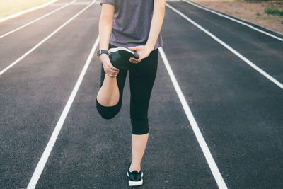 Low section of woman stretching leg on road