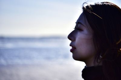 Close-up portrait of young woman looking away against sea