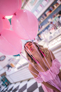 Happy woman holding pink helium balloons while standing in store