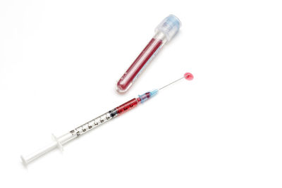 Close-up of medicine leaking from syringe over white background