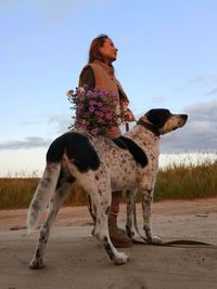 Low angle view of woman standing with dog on land against sky during sunset