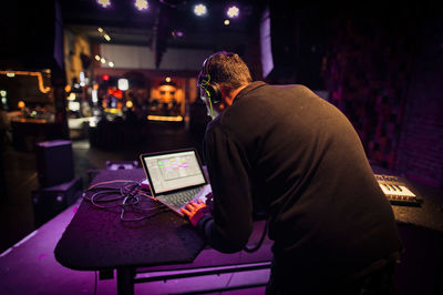 Rear view of man using laptop while standing in nightclub
