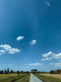 Empty road amidst field against blue sky