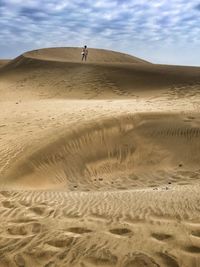 Distant view of man standing on sand dunes at desert