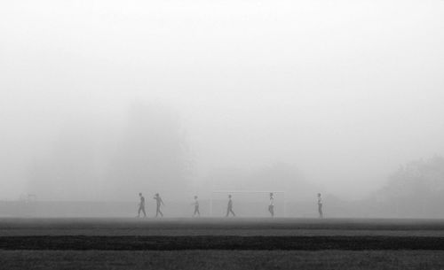 Male friends walking on soccer field during foggy weather