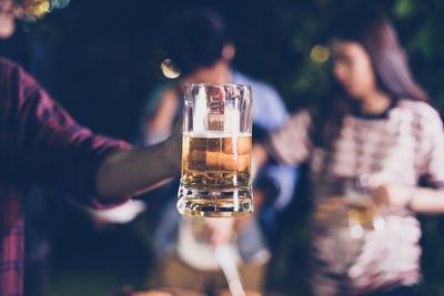 Midsection of man holding beer while standing with friends at backyard during night