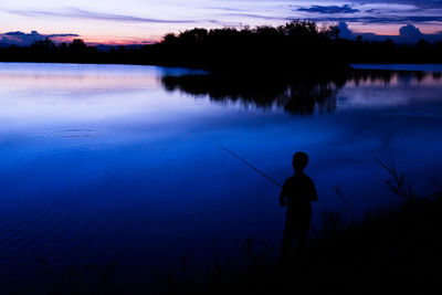 Rear view of silhouette man fishing in lake against sky