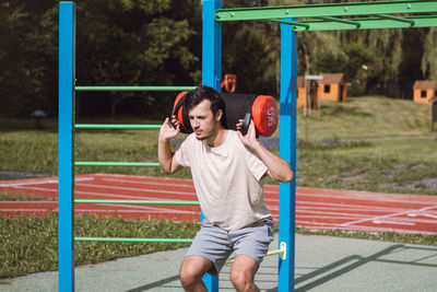 Man with a 10kg dumbbell with water on his shoulders does a squat on a balance beam