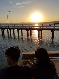 Rear view of people on sea against sky during sunset