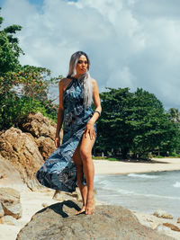 Young trans woman sitting on rock against sky