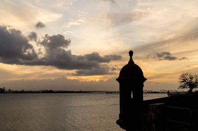 Silhouette building by sea against sky during sunset