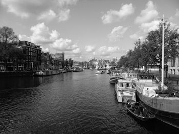 Boats moored at harbor against sky in city