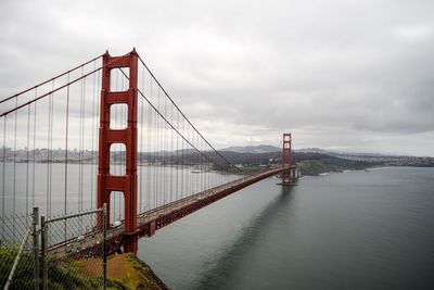 Golden gate bridge over river against cloudy sky