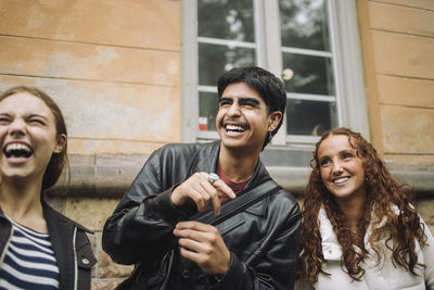 Happy boy laughing with teenage female friends standing against wall