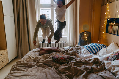 Carefree female friends jumping on bed at home