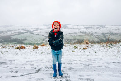 Cute boy sticking out tongue on snow covered mountain road at winter