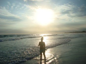 Rear view of woman at beach against sky during sunset