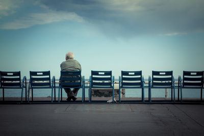 Rear view of man sitting on chair against cloudy sky