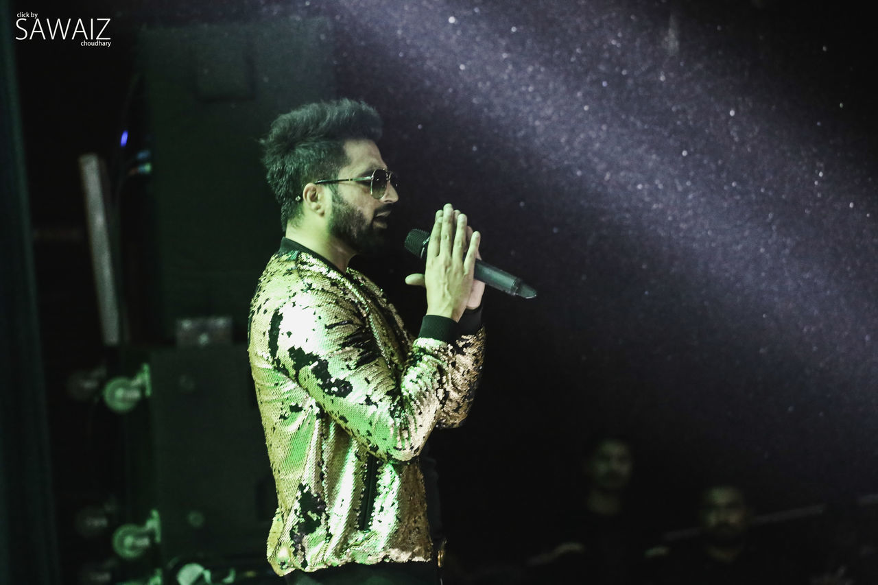 one person, real people, night, young adult, indoors, waist up, holding, men, performance, lifestyles, young men, arts culture and entertainment, standing, green color, leisure activity, focus on foreground, activity, beard, nightlife