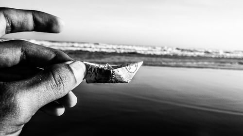 Cropped hand of person holding paper boat by lake