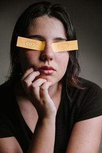Young woman with eyes covered by papers against gray background