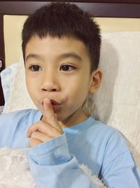 Close-up of boy with finger on lips relaxing on bed