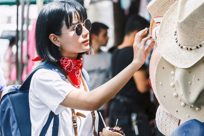 Side view of young woman with backpack shopping for hat in city during sunny day