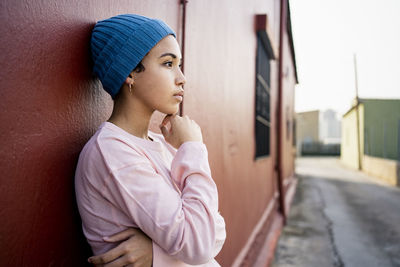 Contemplating woman with hand on chin standing in front of wall