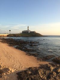 Lighthouse by sea against clear sky