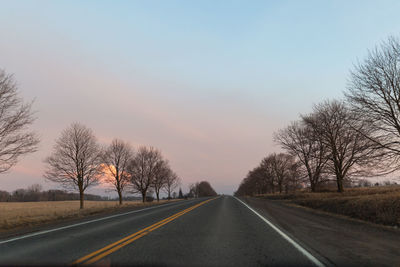 Road by trees against sky during sunset