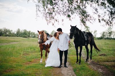 Couple kissing while standing by horses on field