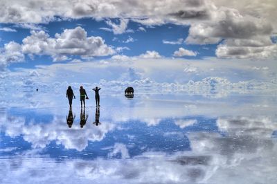 Rear view of friends standing on frozen lake with reflection of cloudy sky
