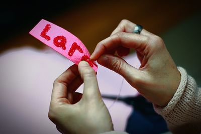 Cropped hands of woman sewing text on pink fabric