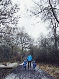 Rear view of family walking on footpath amidst bare trees at forest