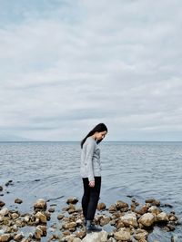 Woman standing on rock by sea against sky