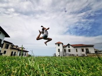 Low angle view of girl jumping on grassy land against sky