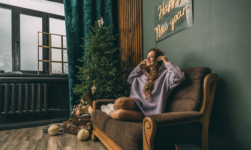 Young girls with headphones listens music, vinyl record, sitting on sofa near glowing christmas tree