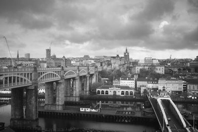 Bridge over river by buildings in city against sky