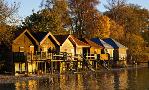 Houses by lake against sky during autumn