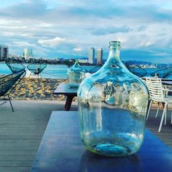 Close-up of water bottle on table by sea against sky