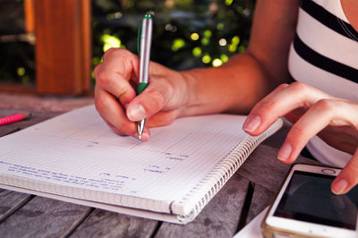 Midsection of woman studying while using smartphone on table