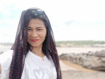 Portrait of beautiful young woman standing on beach against sky