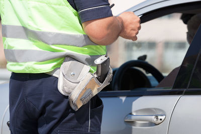 Midsection of police officer with gun standing by car