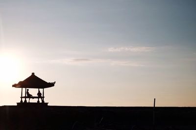 Silhouette people sitting in gazebo on field against sky