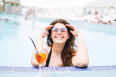Stylish woman plus size body positive in swimsuit and sunglasses with glass of cocktail in pool