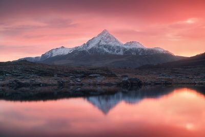 Scenic view of lake by mountains against orange sky