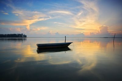 Boat moored in lake against sky during sunset